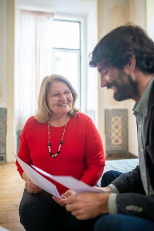 Man and Woman Sitting and Holding Paperwork Smiling