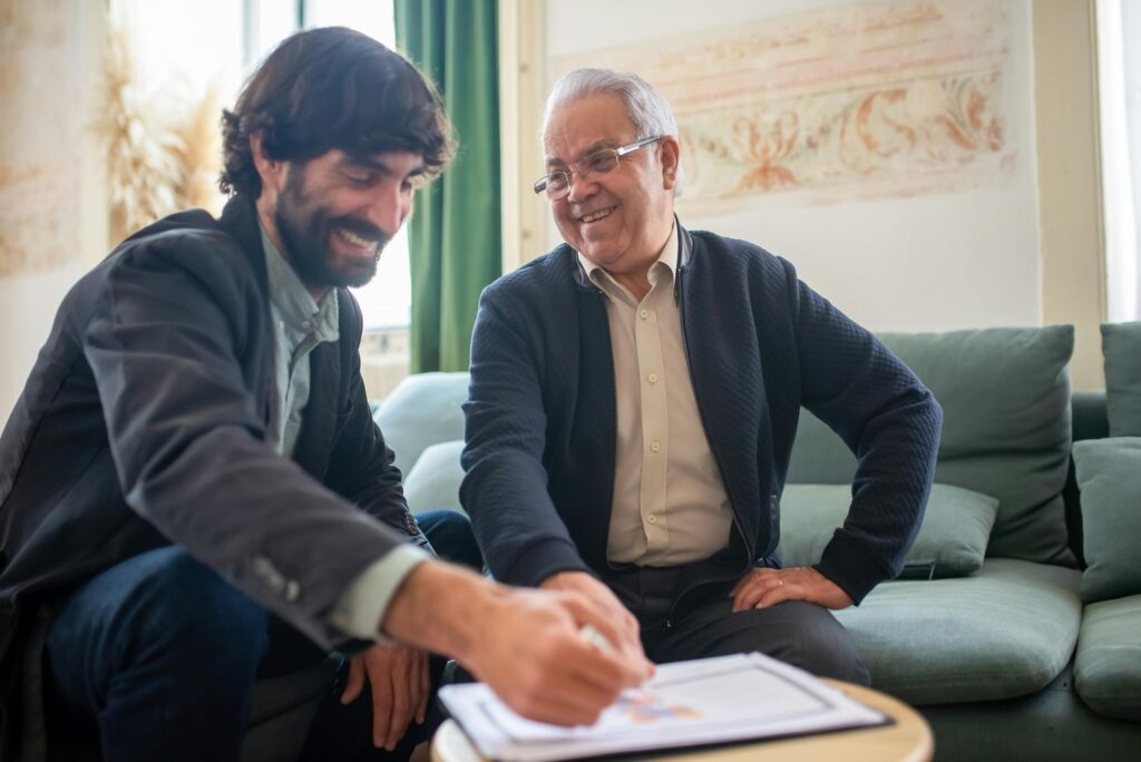 Two Men Smiling While Discussing Paperwork on a Wooden Table