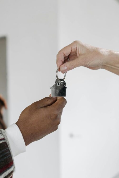 A Person Handing a Key with House Pendant to Another Person