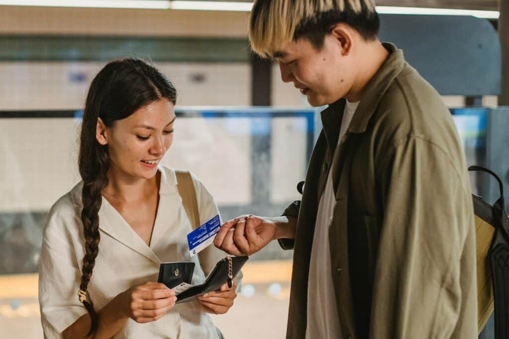 Content Asian couple in casual clothes opening wallet and buying tickets for public subway standing in underground passage