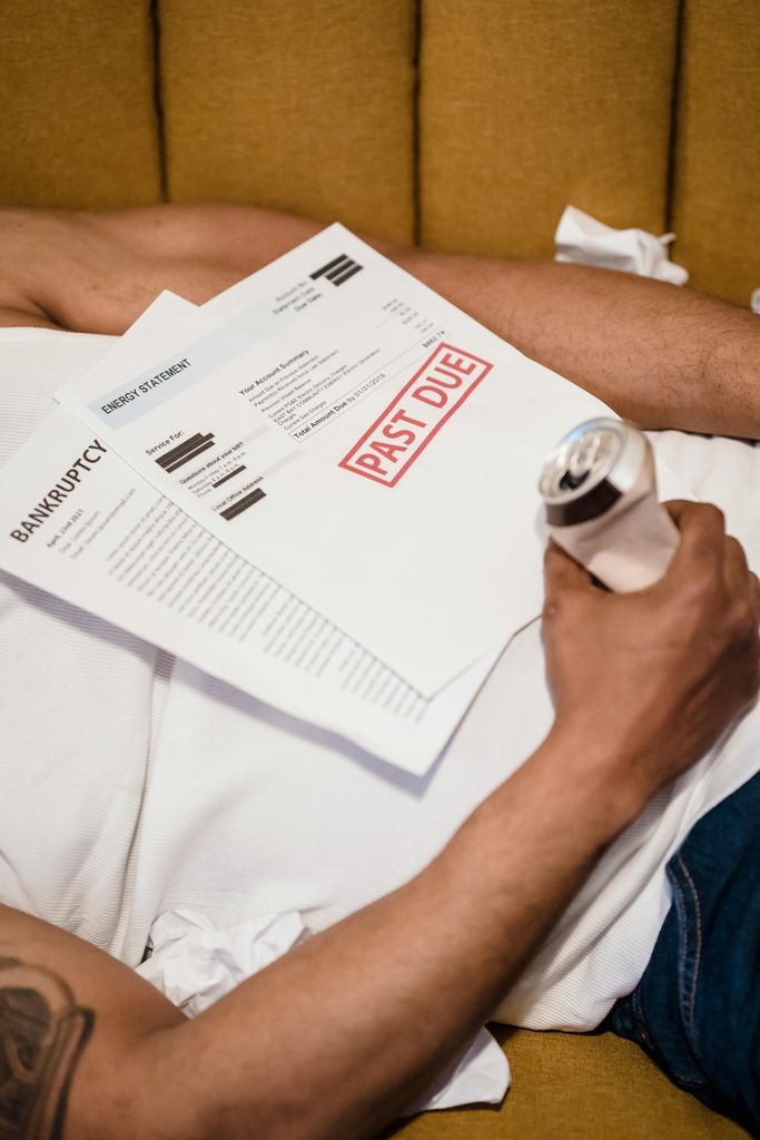 Man Lying with Past Due Letters and Beer in Hands